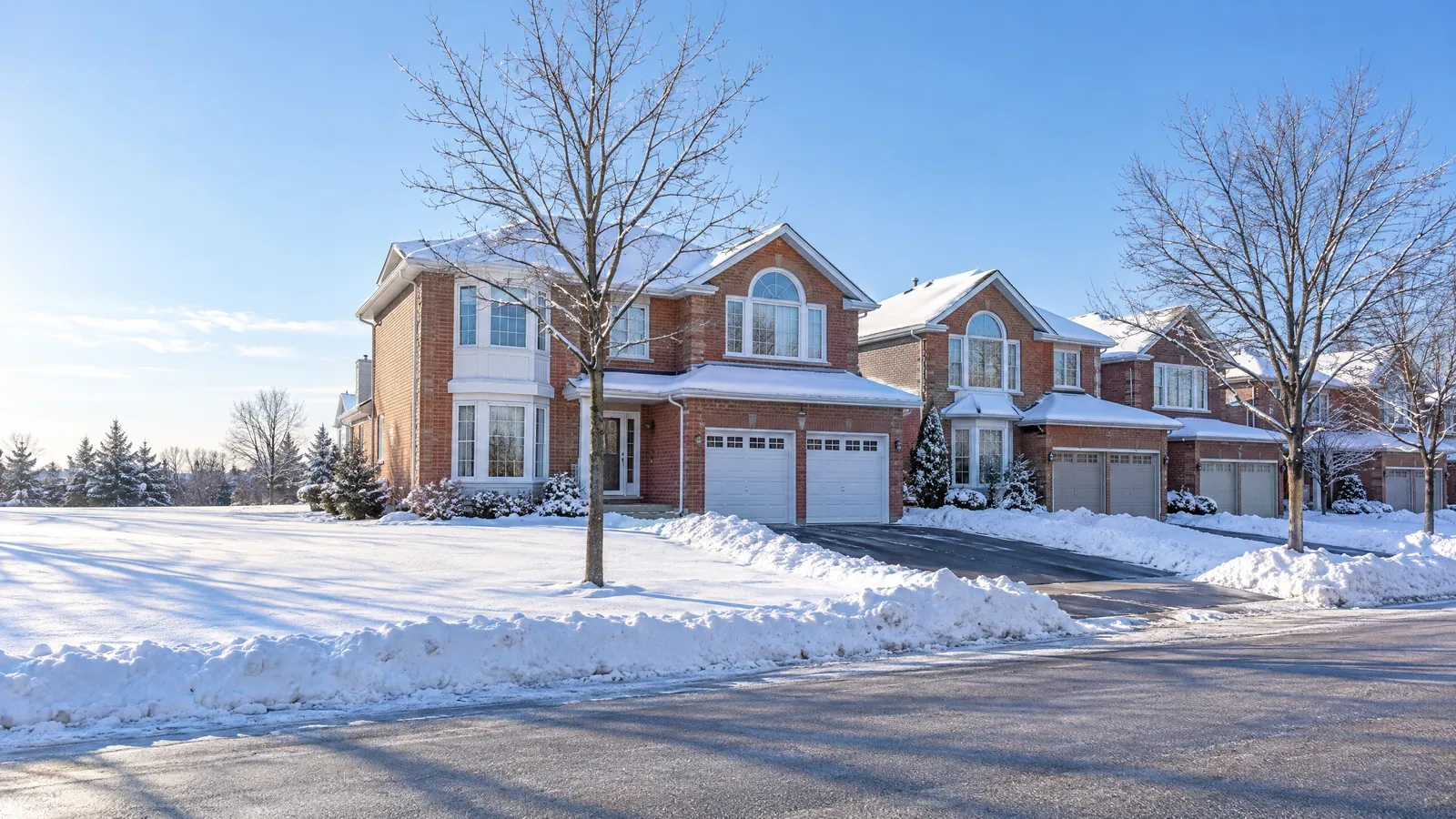Snowy crescent of red-brick two-storey homes with half-round feature windows, bay windows and double garages under a clear winter sky