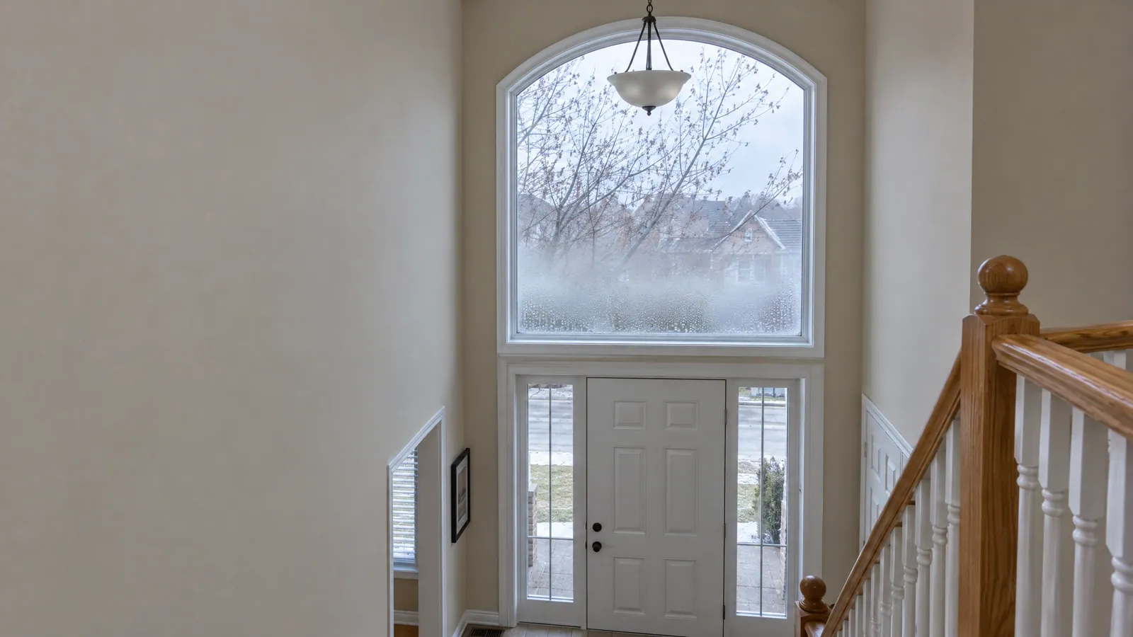 Two-storey foyer with a tall arched window clouded by fog between the panes, above a white front door with clear sidelights